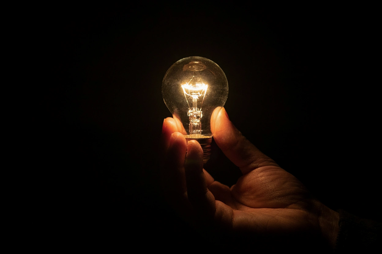 Main tenant une ampoule LED allumée dans une pièce sombre